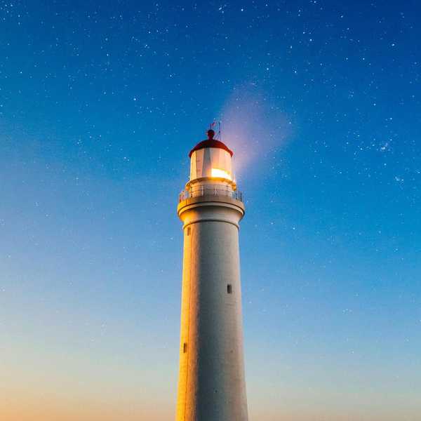 星空の下で明るく照らす灯台と海