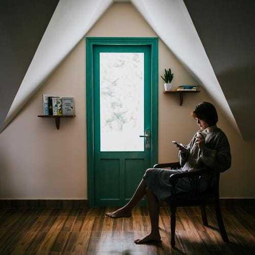 木の床が美しい部屋の椅子に座りながら本を読む女性の画像