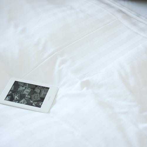 清潔で真っ白なベッドシーツの上に埋まるキンドルのホワイトモデル